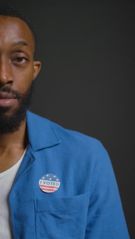 Vertical-Video-Close-Up-Portrait-Shot-Of-Man-Putting-I-Voted-Sticker-On-Shirt-In-American-Election